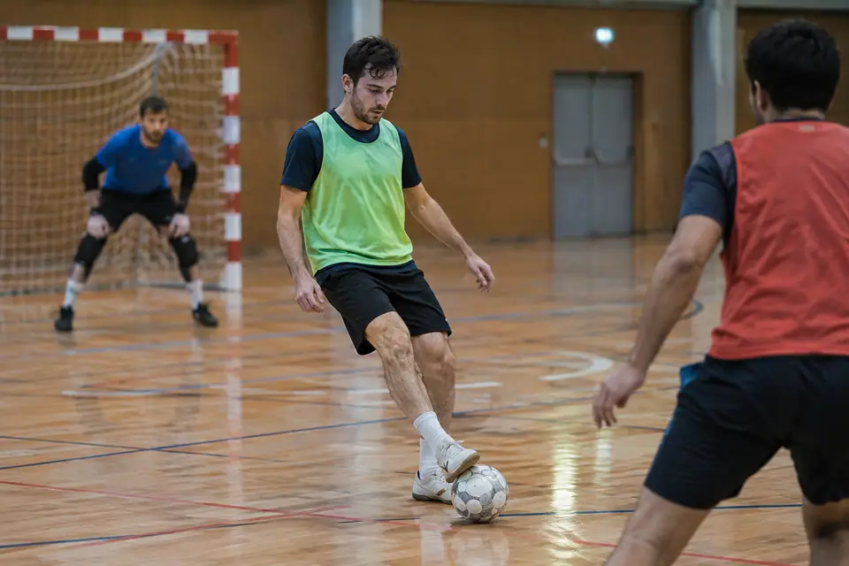 Un joueur de futsal contrôle le ballon de la semelle sur le parquet d'un gymnase municipal