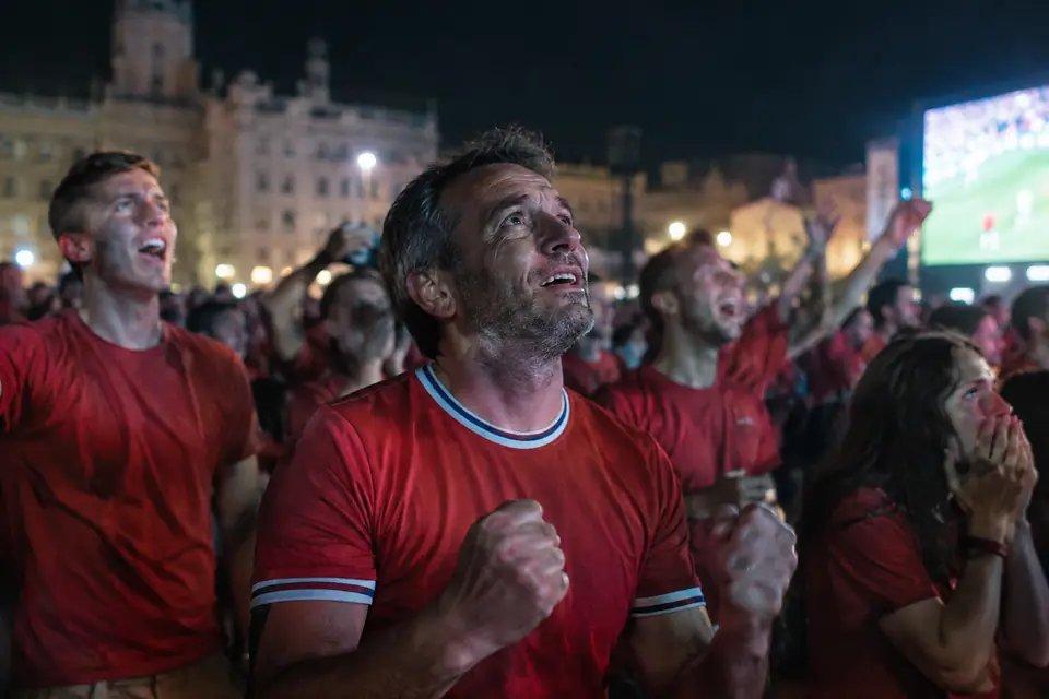 Supporter en maillot de foot rouge au milieu d'une foule devant un écran géant la nuit