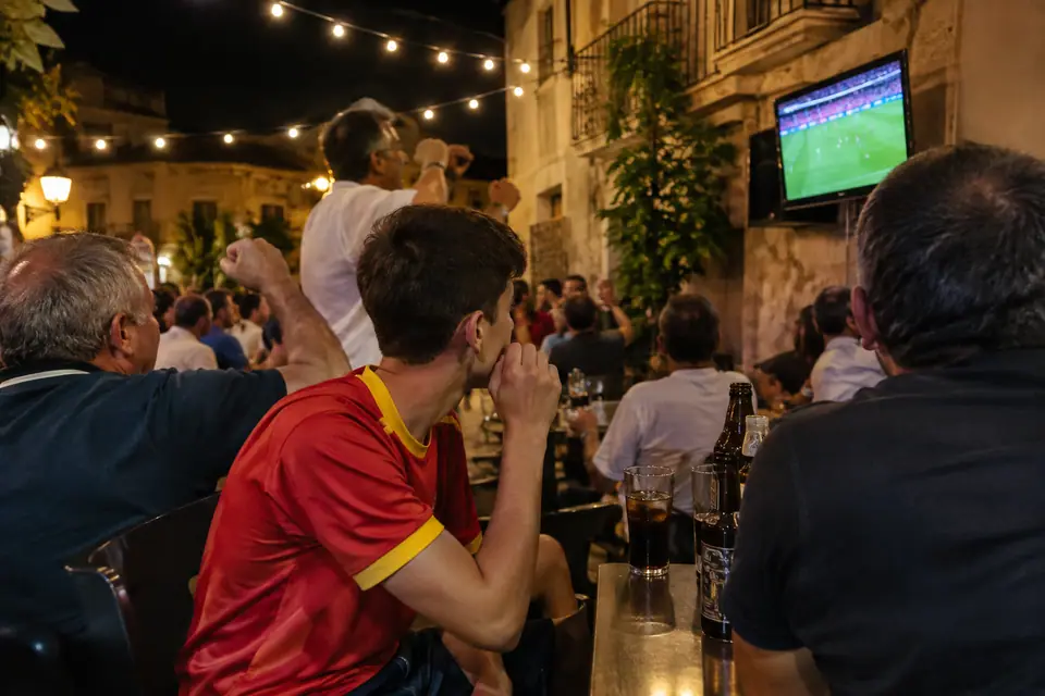 Adolescent en maillot de foot rouge regardant un match sur une terrasse de bar espagnole le soir