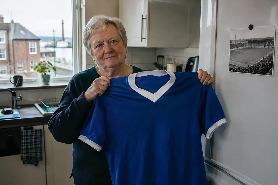 Femme tenant un maillot de foot bleu royal rétro dans la cuisine d'une maison anglaise