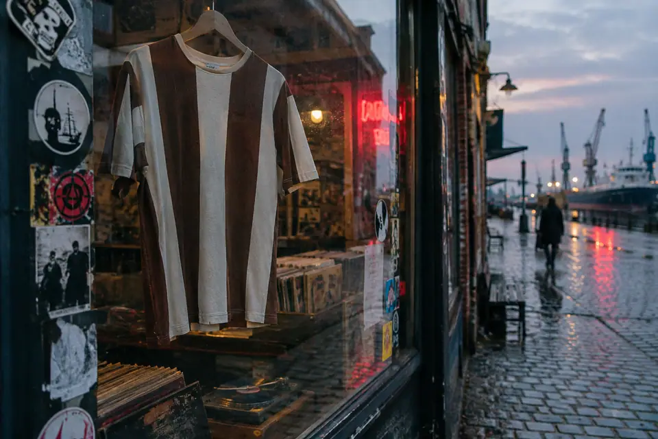 Maillot de foot marron et blanc suspendu dans la vitrine d'un disquaire de quartier portuaire
