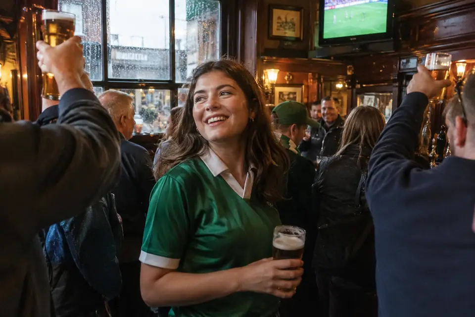 Supportrice souriante en maillot de foot vert rétro dans un pub chaleureux un soir de match