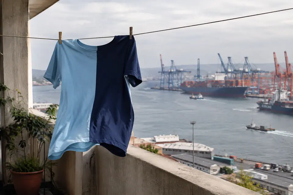 Maillot de foot rétro moitié bleu ciel, moitié bleu marine séchant sur un balcon face au port