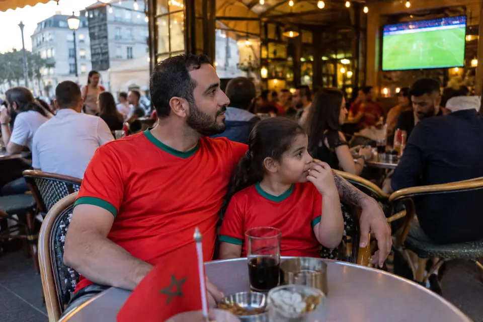 Un père et sa fille en maillots rouges à finitions vertes regardent un match en terrasse