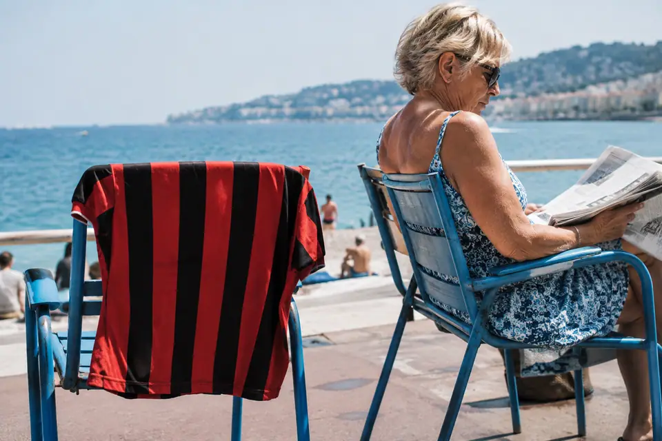 Maillot de foot rétro à rayures rouges et noires posé sur une chaise bleue au bord de la mer