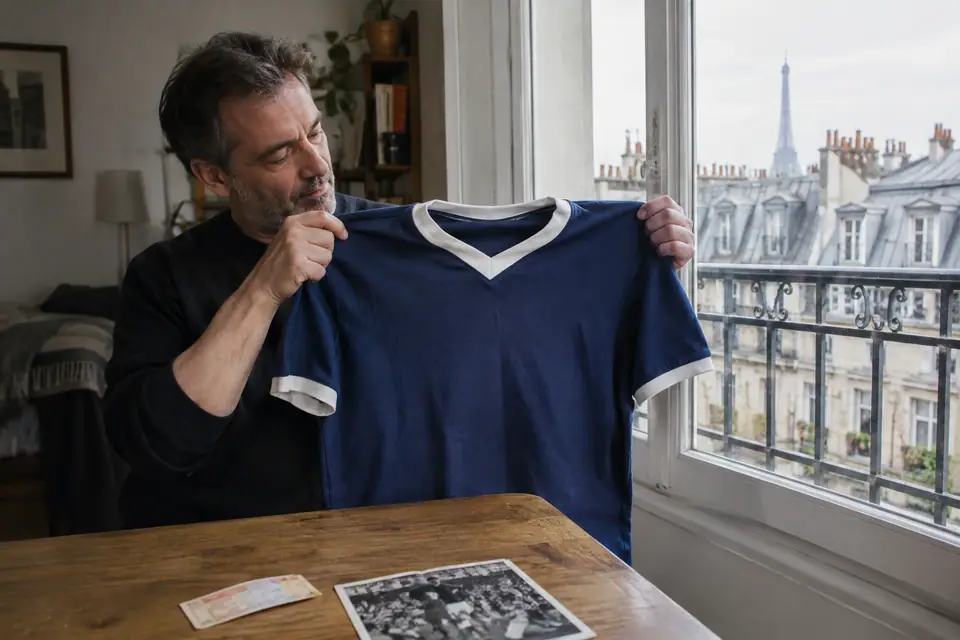 Homme tenant un maillot de foot rétro bleu marine dans un appartement parisien avec vue sur les toits