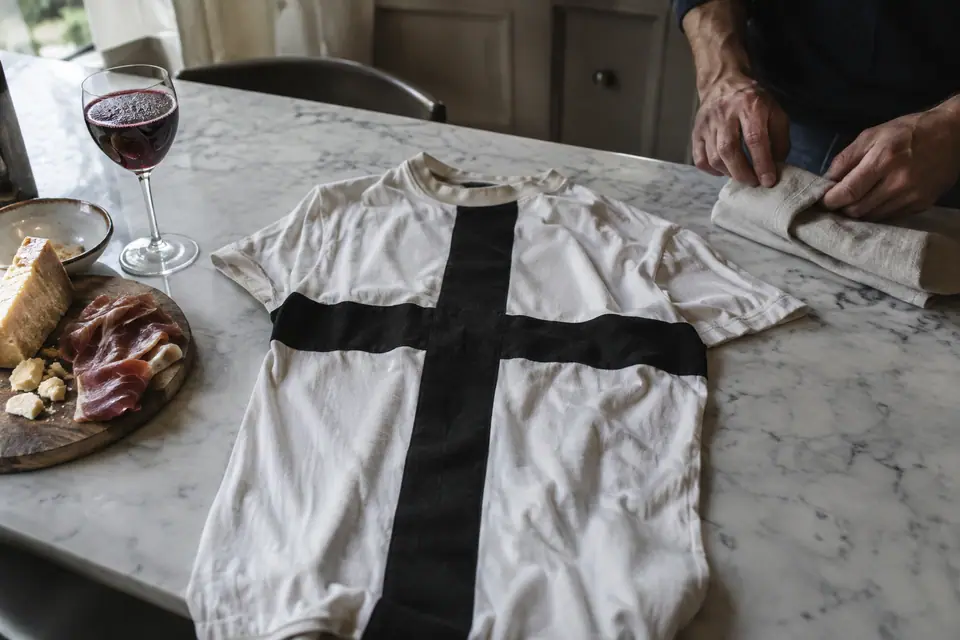 Maillot de foot blanc à croix noire posé sur un comptoir de cuisine à côté de fromage et de jambon