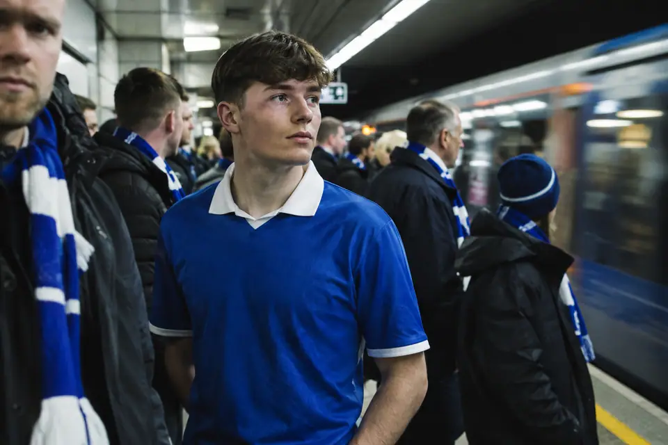 Jeune supporter en maillot de foot bleu royal rétro sur un quai de métro bondé un jour de match