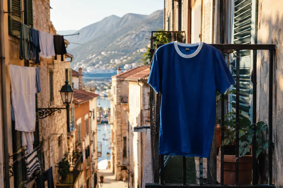 Maillot de foot rétro bleu roi suspendu à un balcon dans une ruelle de port méditerranéen