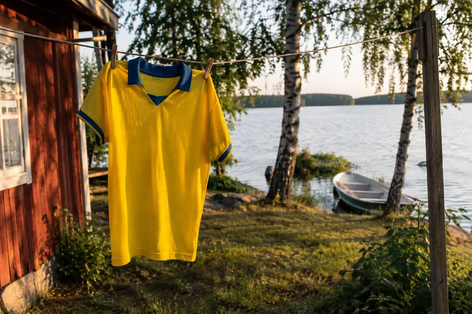 Maillot de foot jaune à col bleu séchant sur un fil à linge près d'un lac suédois