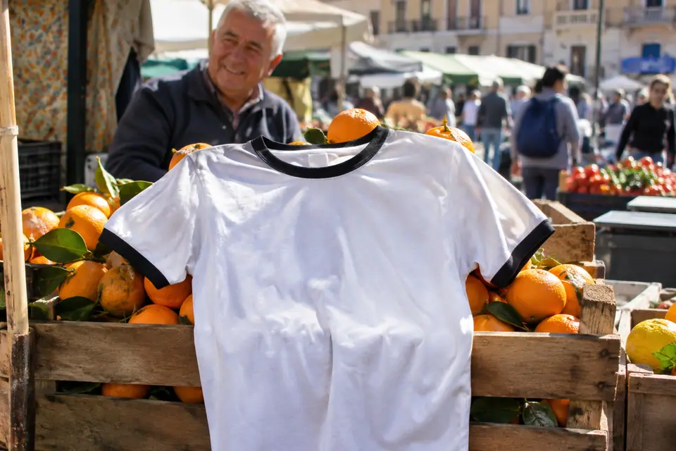 Maillot de foot blanc à finitions noires posé sur une cagette d'oranges dans un marché espagnol
