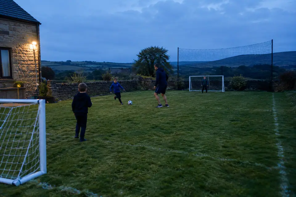 Un grand jardin aménagé en petit terrain de foot avec lignes blanches, deux buts et un projecteur au crépuscule