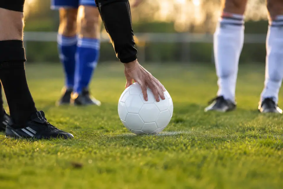 Un arbitre pose un ballon de match neuf sur le rond central d'un terrain en herbe, un dimanche après-midi