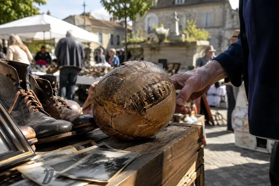 Vieux ballon de foot en cuir brun à lacets posé sur une caisse en bois dans une brocante de village