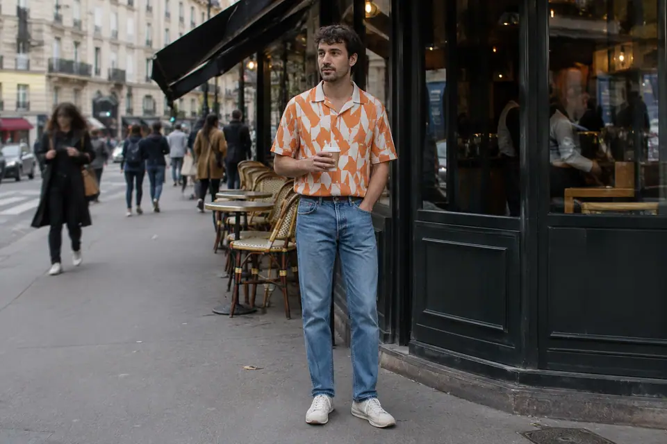 Homme en maillot de foot rétro orange rentré dans un jean droit devant un café en ville