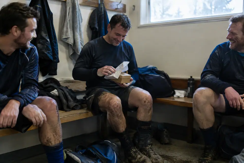 Homme d'une quarantaine d'années qui ouvre un cadeau dans le vestiaire d'un club amateur après le match