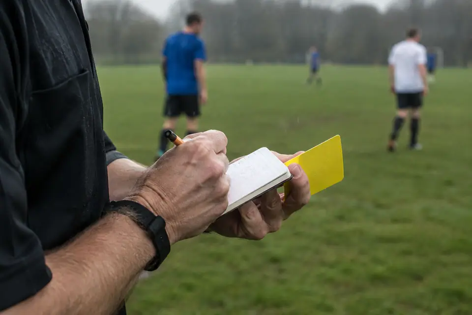 Les mains d'un arbitre amateur notent un avertissement dans un carnet sous la pluie, carton jaune entre les doigts