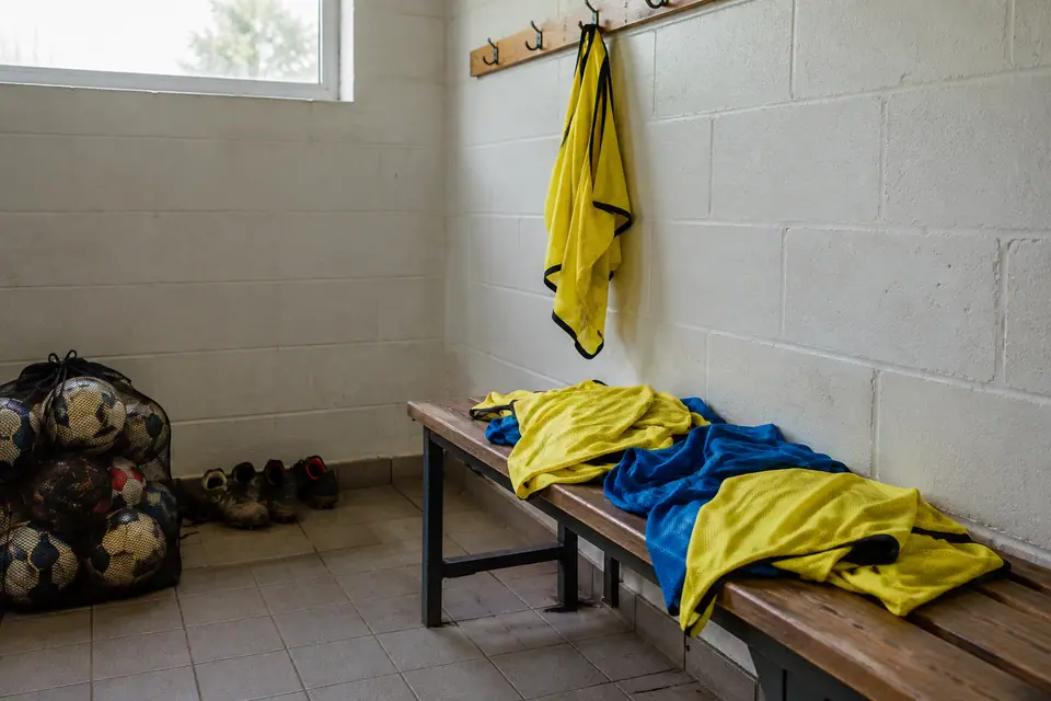 Chasubles jaunes et bleues qui sèchent sur un banc de vestiaire de club amateur, ballons au sol