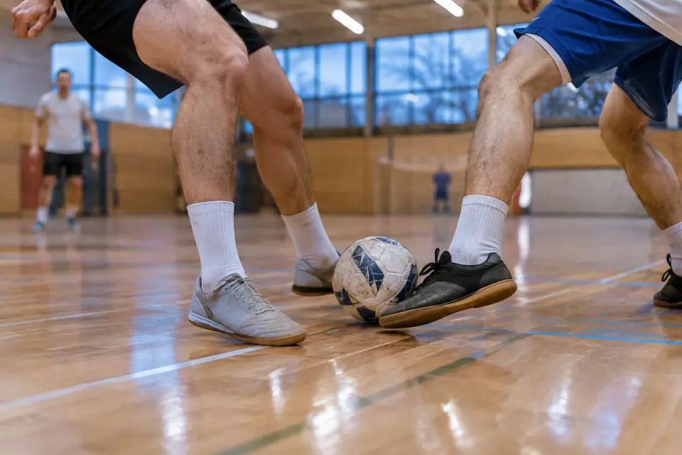 Pieds de deux joueurs de futsal en chaussures à semelle gomme se disputant le ballon sur un parquet