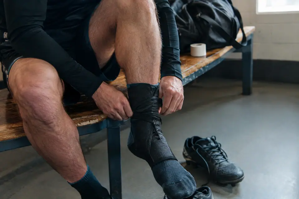Joueur amateur serrant une chevillère à lacets noire sur sa cheville avant d'enfiler ses chaussures de foot