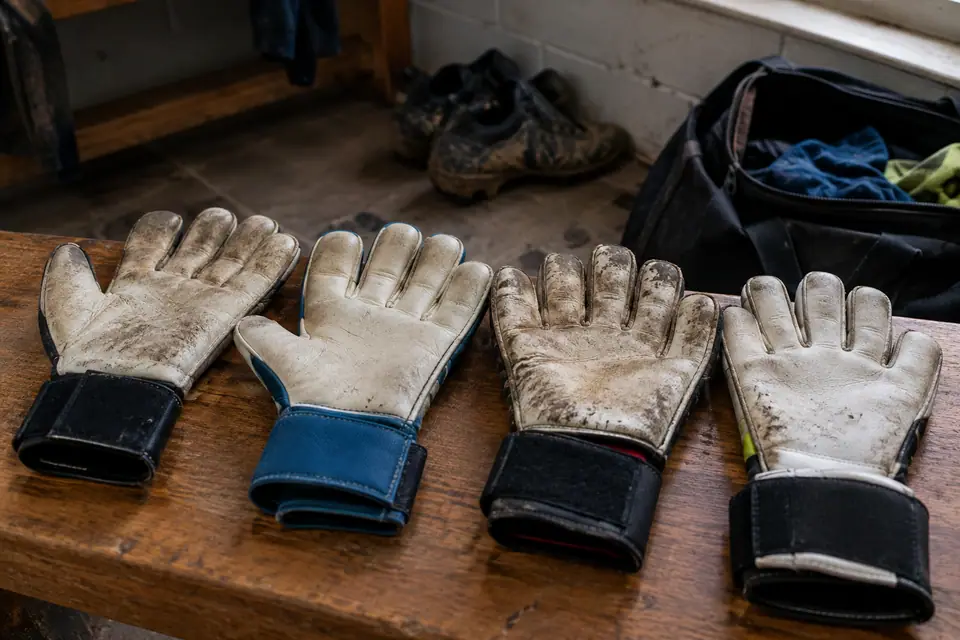 Quatre gants de gardien de coupes différentes posés paume vers le haut sur un banc de vestiaire