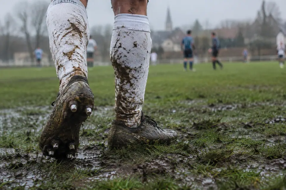 Chaussures de foot à crampons vissés enfoncées dans un terrain boueux sous la pluie d'automne