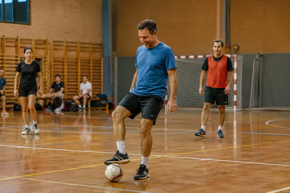 Adultes débutants disputant une séance de futsal loisir dans un gymnase municipal en soirée