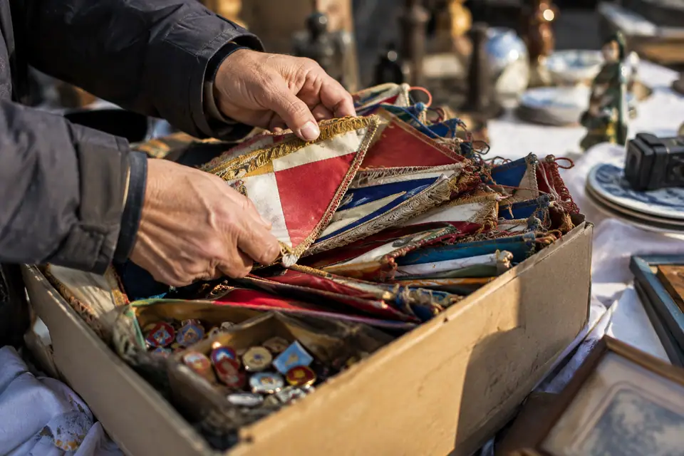 Des mains trient de vieux fanions de foot et des pin's dans une boîte à chaussures sur un stand de brocante