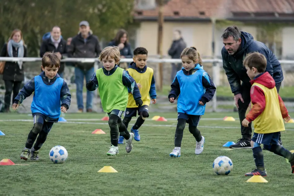 Des enfants de six ans jouent au ballon entre des coupelles colorées pendant une séance du samedi matin