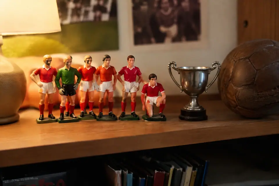 Une étagère en bois avec une rangée de petites figurines de footballeurs, une coupe et un vieux ballon