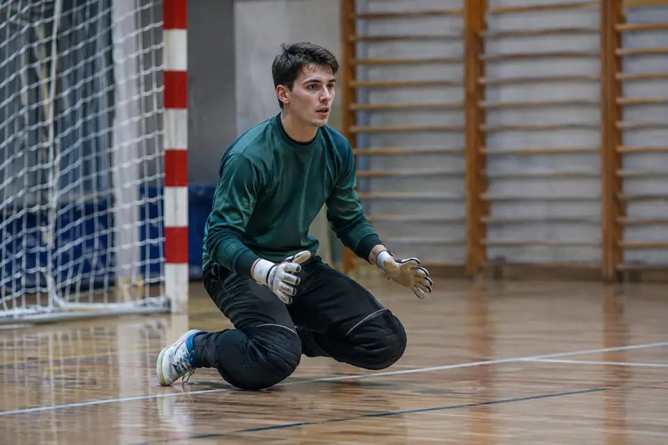 Gardien de futsal à genoux sur le parquet d'un gymnase, avec genouillères et pantalon de gardien