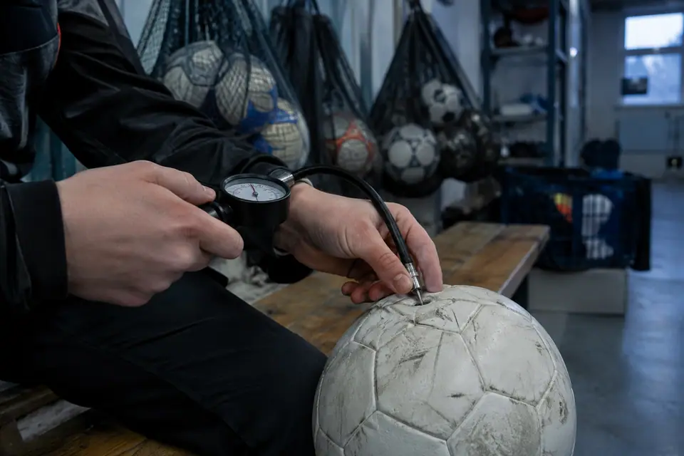 Mains d'un éducateur qui gonfle un ballon de foot avec une pompe à manomètre dans un local de club