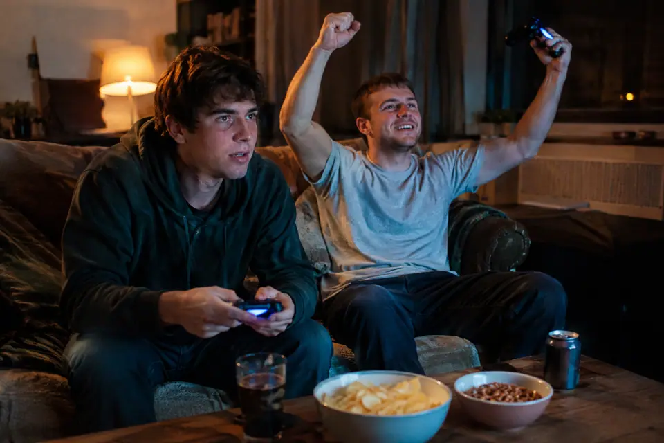 Deux frères assis sur un canapé jouent à un jeu vidéo de foot, éclairés par la lumière de la télévision