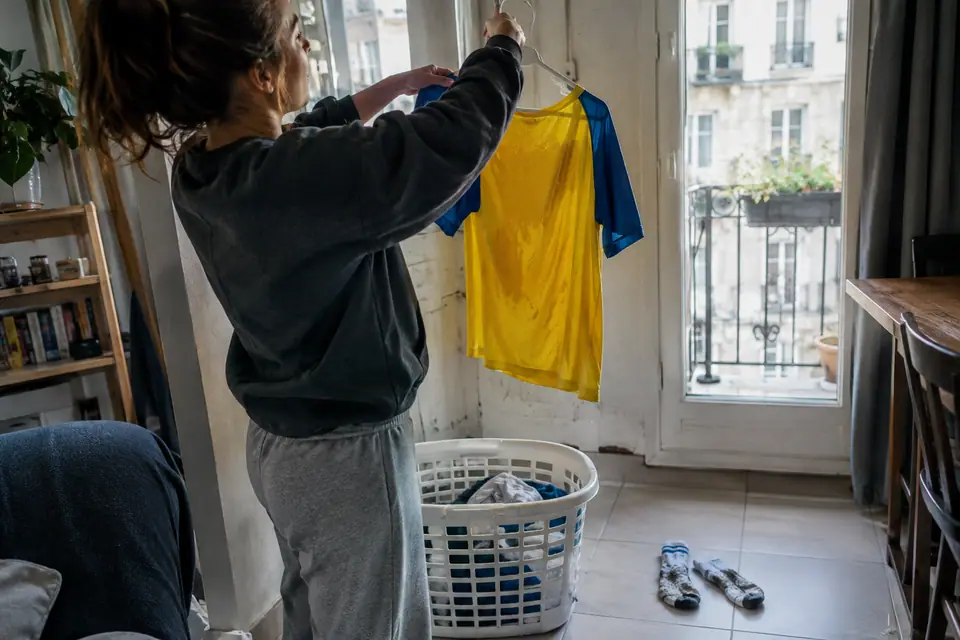 Une femme suspend à un cintre un maillot de foot jaune retourné, à côté d'un panier de linge