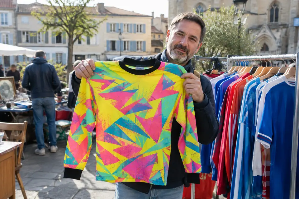 Un collectionneur montre un maillot de gardien rétro aux motifs fluo sur un stand de brocante