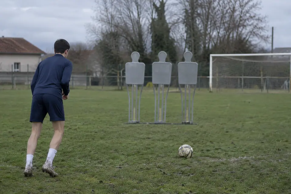 Trois mannequins coup franc alignés sur un terrain en herbe, un joueur amateur place le ballon devant eux