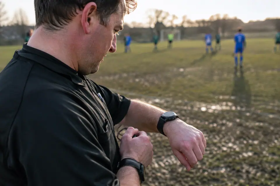 Un arbitre amateur regarde sa montre digitale en fin de match, une seconde montre visible à l'autre poignet