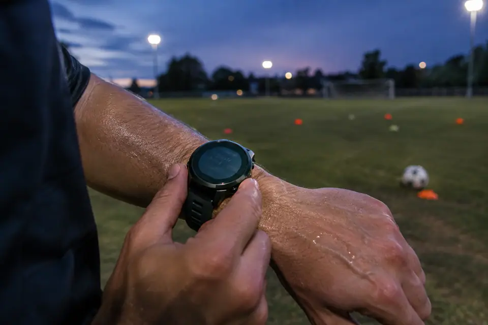 Un joueur amateur consulte sa montre GPS au poignet après un entraînement sur un terrain municipal