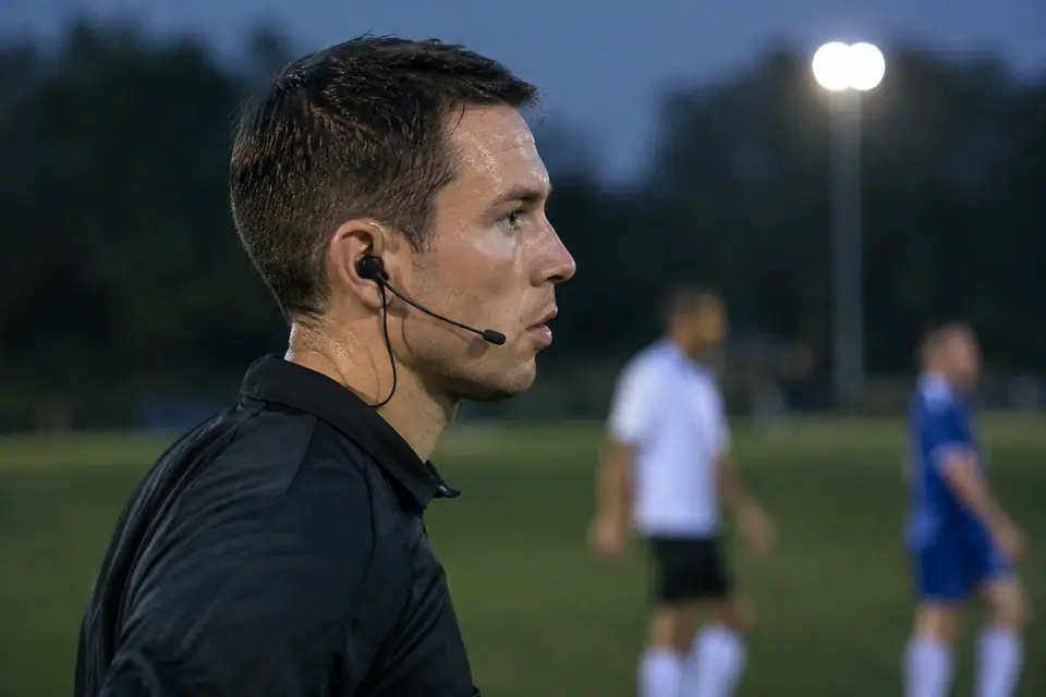 Profil d'un arbitre amateur portant une oreillette discrète et un micro le long de la joue sous les projecteurs