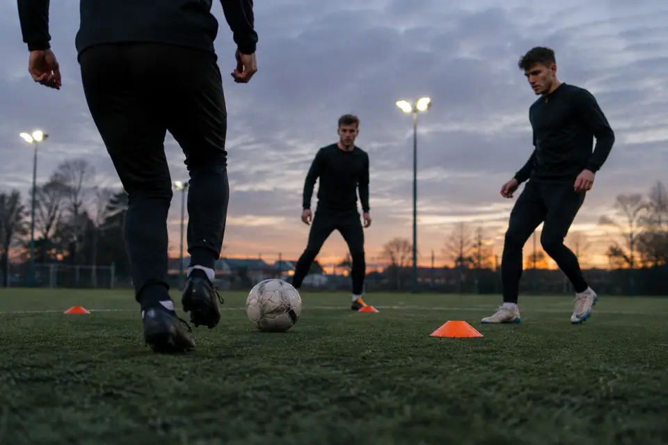 Trois joueurs amateurs en pantalons d'entraînement noirs fuselés font des passes entre des coupelles au crépuscule