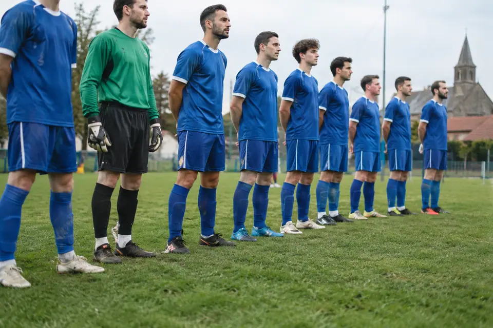 Joueurs amateurs alignés avant le coup d'envoi, avec des chaussures de foot différentes selon les postes