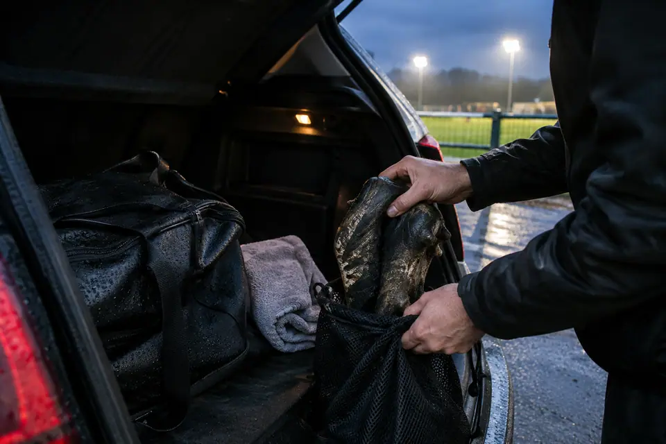 Mains d'un joueur rangeant des crampons boueux dans un sac en filet, dans le coffre d'une voiture
