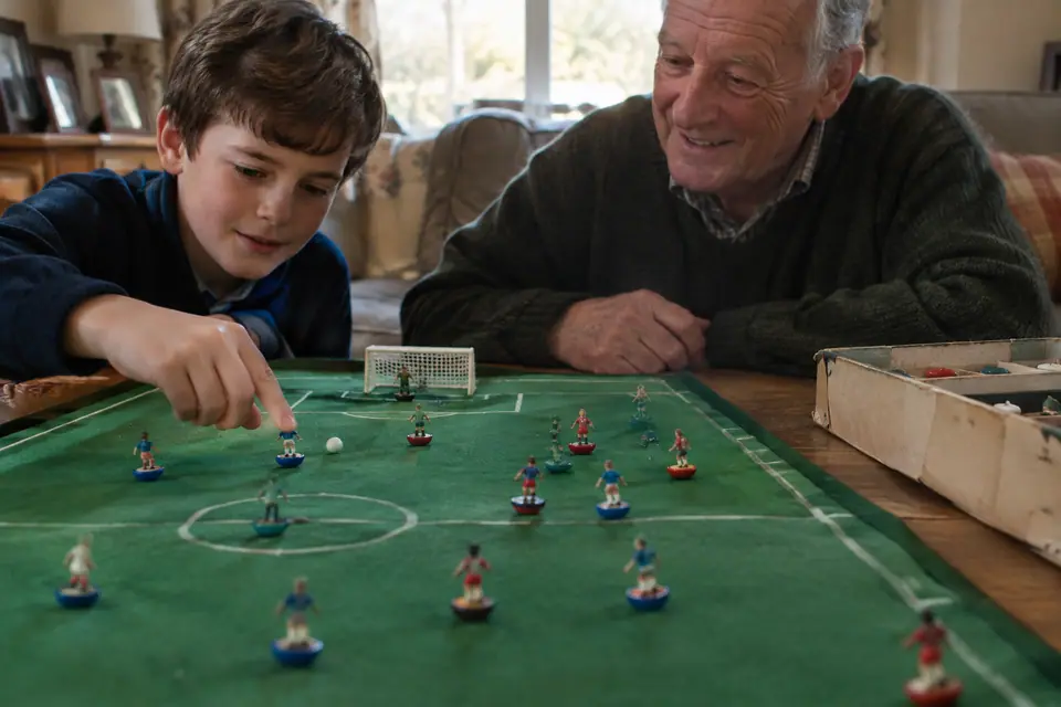 Un enfant s'apprête à donner une pichenette à une figurine de football de table sous le regard de son grand-père