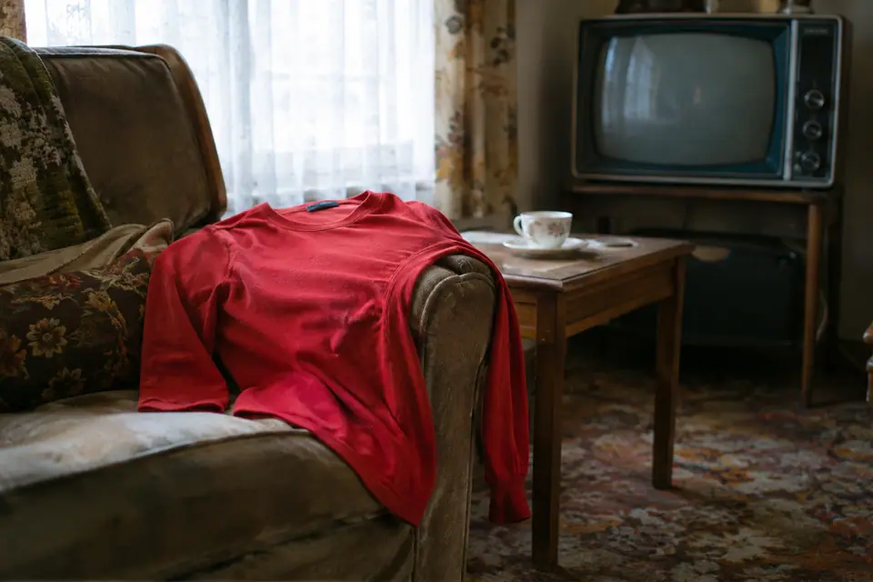 Maillot de foot rouge rétro à manches longues posé sur un fauteuil près d'un vieux téléviseur