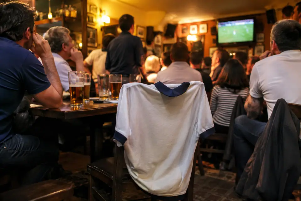 Maillot de foot blanc rétro à col bleu marine accroché à une chaise dans un pub anglais