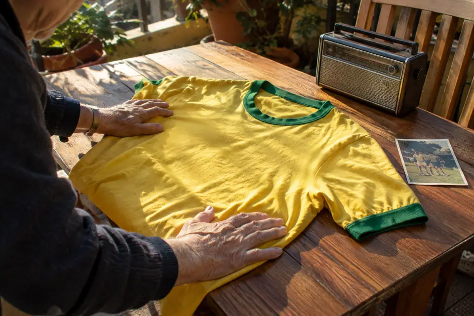 Mains d'un homme âgé lissant un maillot de foot jaune à col vert sur une table en bois