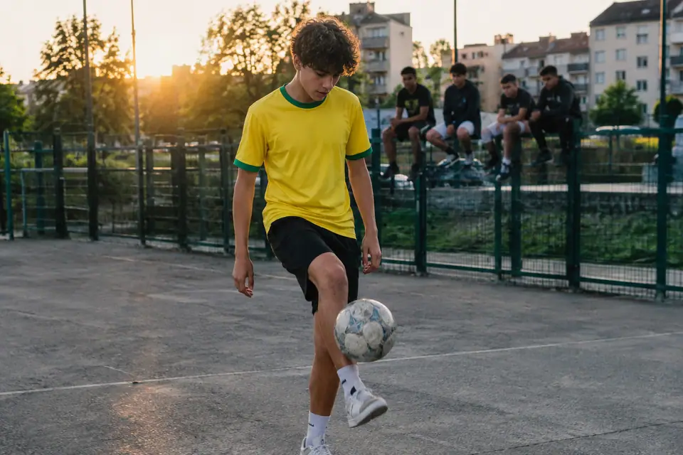 Adolescent en maillot de foot jaune à finitions vertes jonglant sur un terrain de quartier