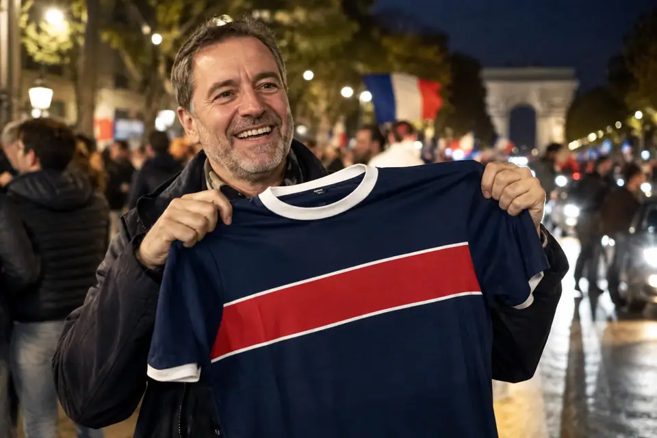 Homme brandissant un maillot de foot bleu marine à bande rouge dans une rue de Paris la nuit