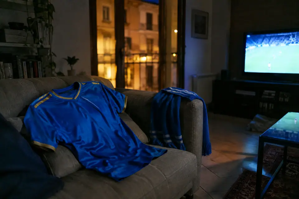 Maillot de foot bleu azur posé sur un canapé devant une télévision allumée, la nuit