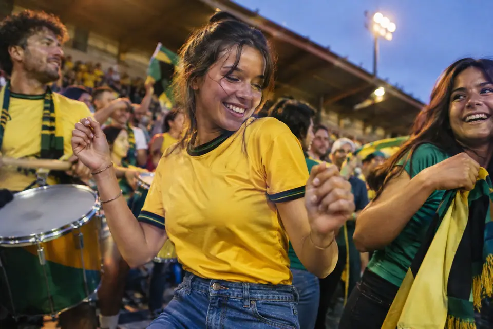 Supportrice souriante en maillot de foot jaune à finitions vertes et noires dansant en tribune